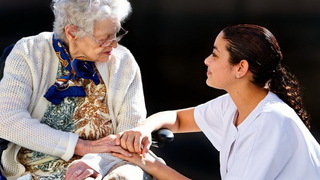 Foto: Pflegerin hält die Hände einer Seniorin im Rollstuhl