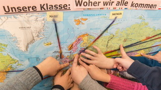 Foto:  Kinder zeigen auf einer Weltkarte, aus welchen Ländern sie kommen.