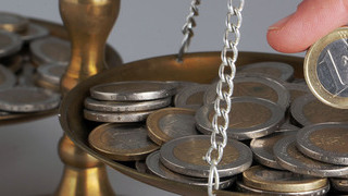 Foto: Eine Hand legt eine Euro-Münze auf eine Waage