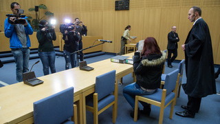 Foto: Angeklagte sitzt  in einem Gerichtssaal und wird von Fotografen und Kamerateams aufgenommen