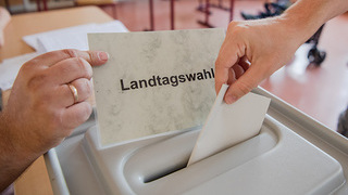 Foto:  Ein Wähler steckt seinen Wahlzettel in die Wahlurne
