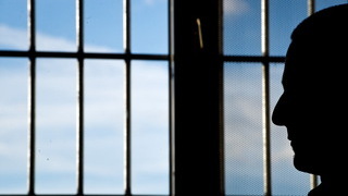 Foto: Gefängnisinsasse sitzt  in einer Justizvollzugsanstalt vor einem vergitterten Fenster