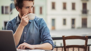 Foto: Ein Mann sitzt mit einem Laptop in einem Strassencafe