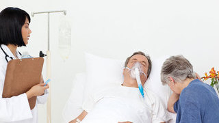 Foto: Ehefrau mit Arzt am Krankenbett