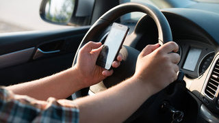 Foto: Handy in der Hand beim Auto fahren