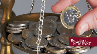 Foto: Eine Hand legt eine Euro-Münze auf eine Waage